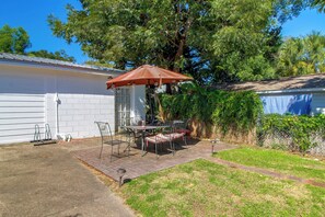 A patio with a table and chairs, a red umbrella, and a white building in the background. - 2 Mi to Dtwn Pensacola: Historic Home w/ Patio! (Pensacola)