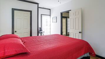 Une chambre avec un grand lit, deux portes, un ventilateur de plafond et une fenêtre avec des stores.