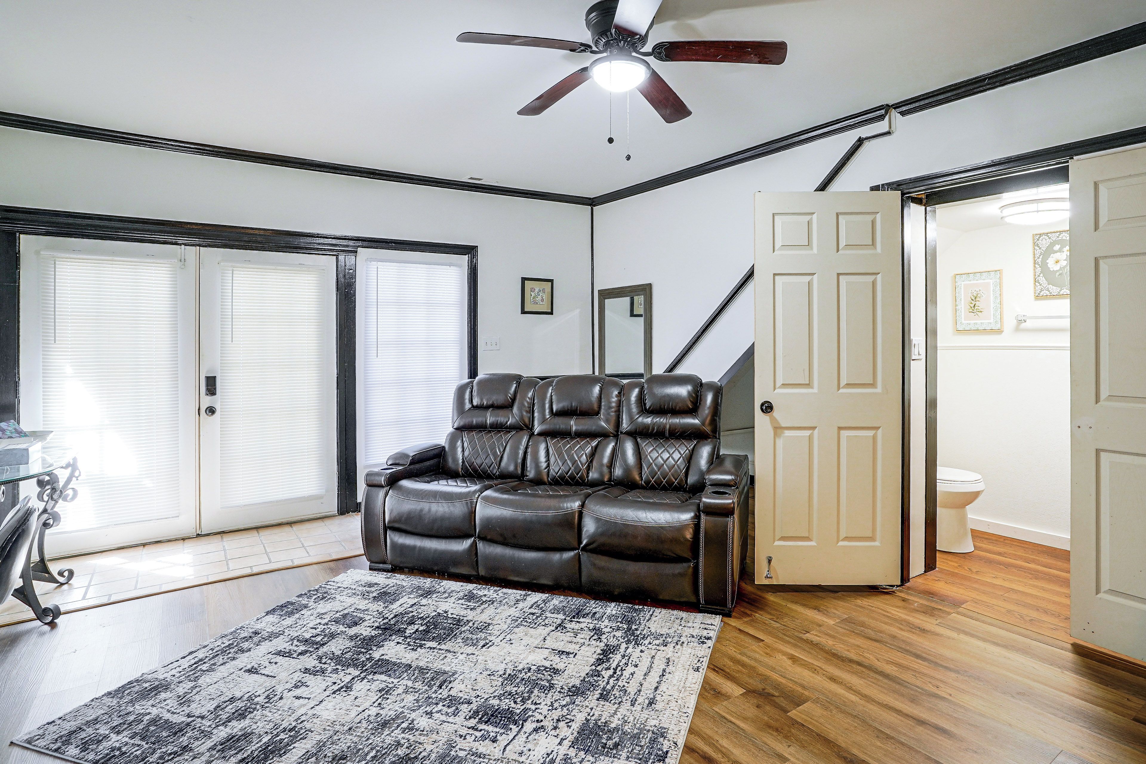 A room with a ceiling fan, a leather recliner, a patterned rug, and a wooden floor.
