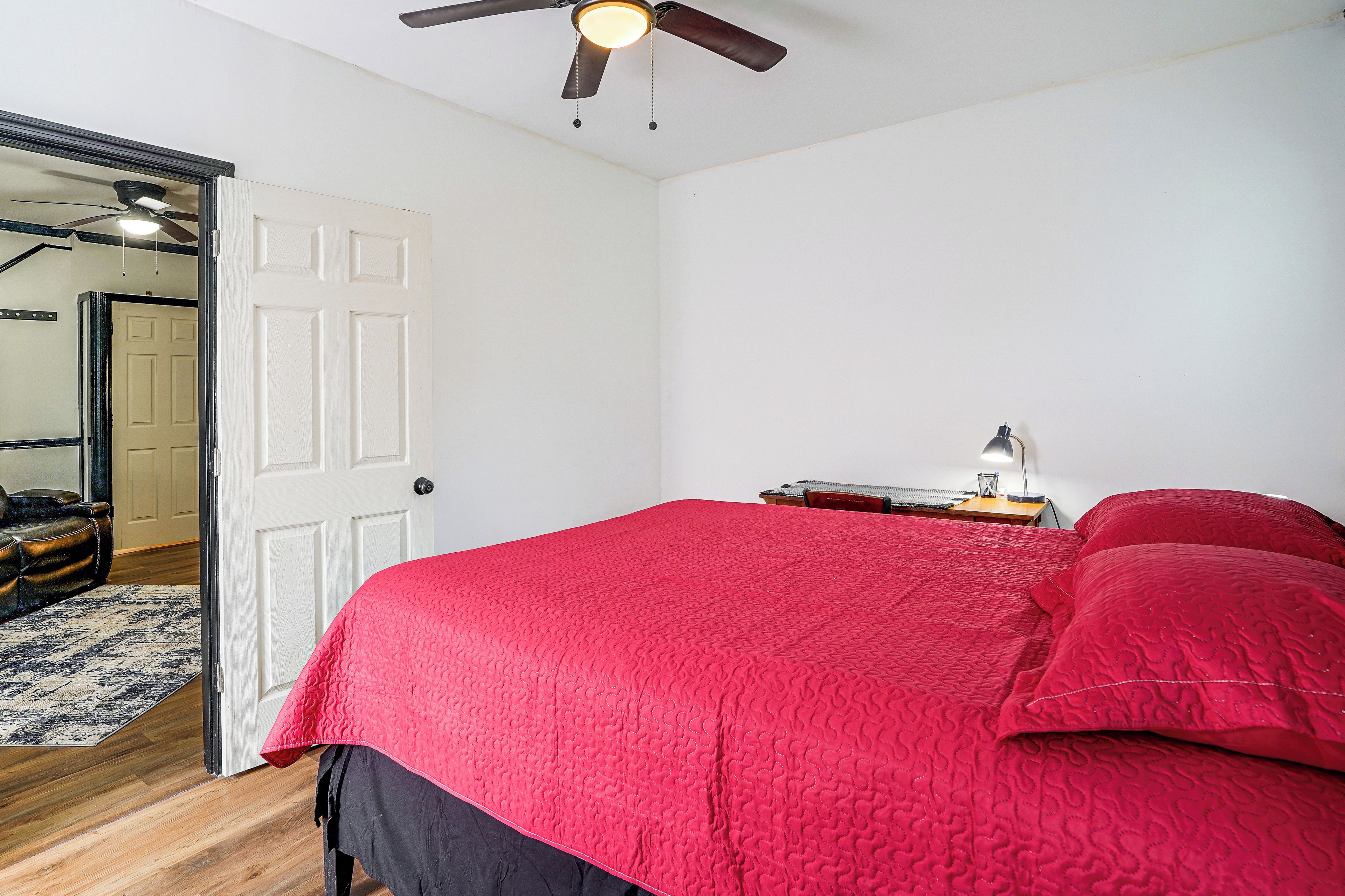 Une chambre à coucher avec un lit, un ventilateur de plafond, une porte et une petite table avec une lampe.
