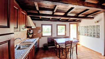 Una cucina con travi in legno, paraschizzi in ceramica, un lavandino e un tavolo da pranzo con sedie.