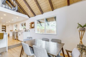 A spacious dining area with a high ceiling and wooden beams, a kitchen with modern appliances, and a view of the outdoors through large windows. - Mtn-view Cabin Escape in Heart of Grand Lake (Grand Lake)