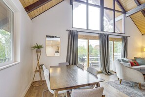 A spacious room with a large dining table, a sofa, and a view of the outdoors through large windows. - Mtn-view Cabin Escape in Heart of Grand Lake (Grand Lake)