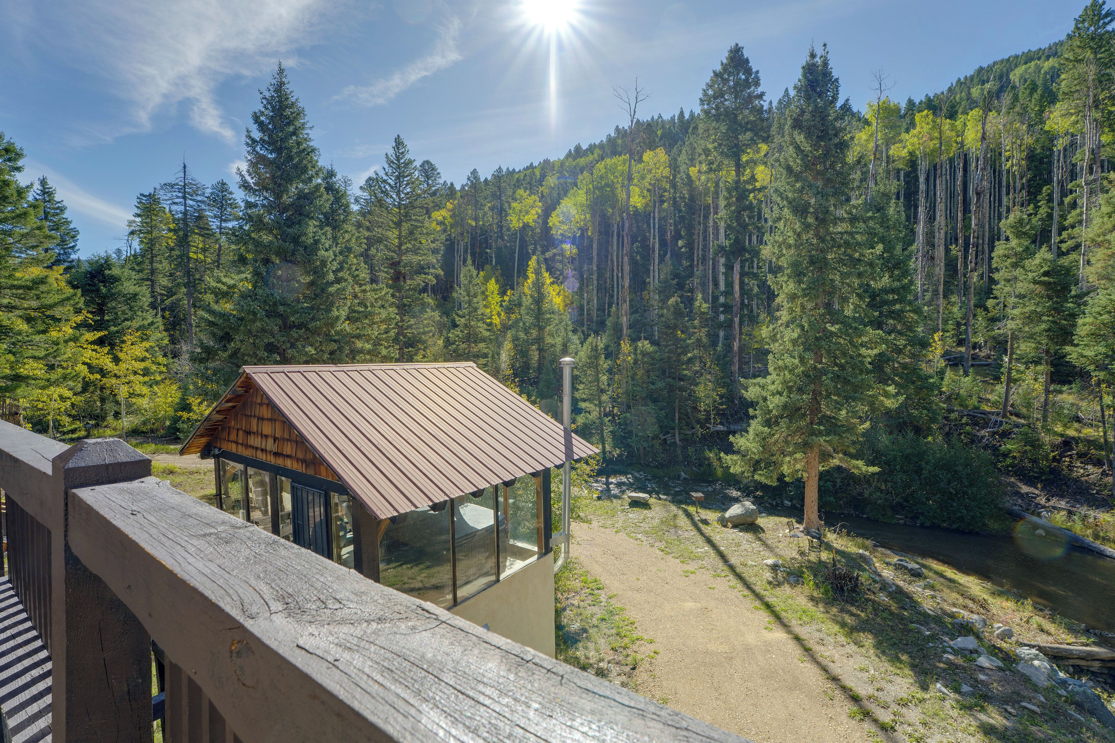 A cabin with a metal roof and glass walls, surrounded by a forest and a river.
