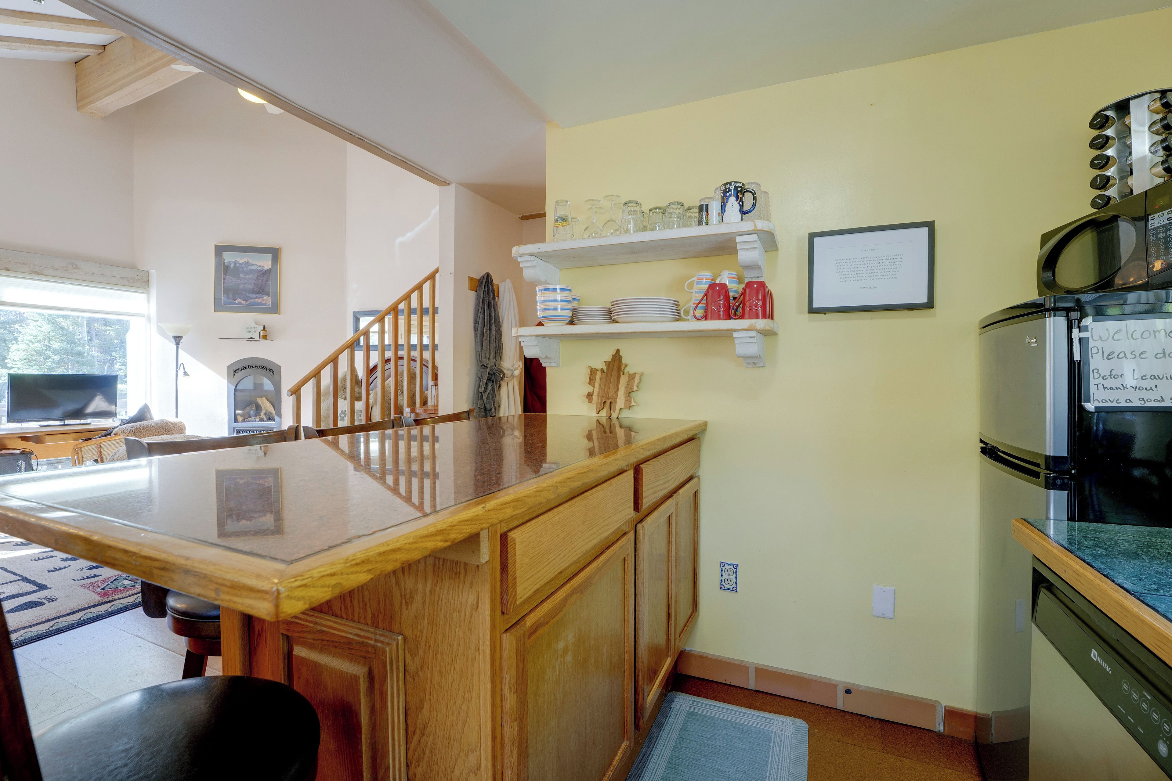 A kitchen with wooden cabinets, a microwave, and a refrigerator. There is a wooden counter and a dining area with a table and chairs.