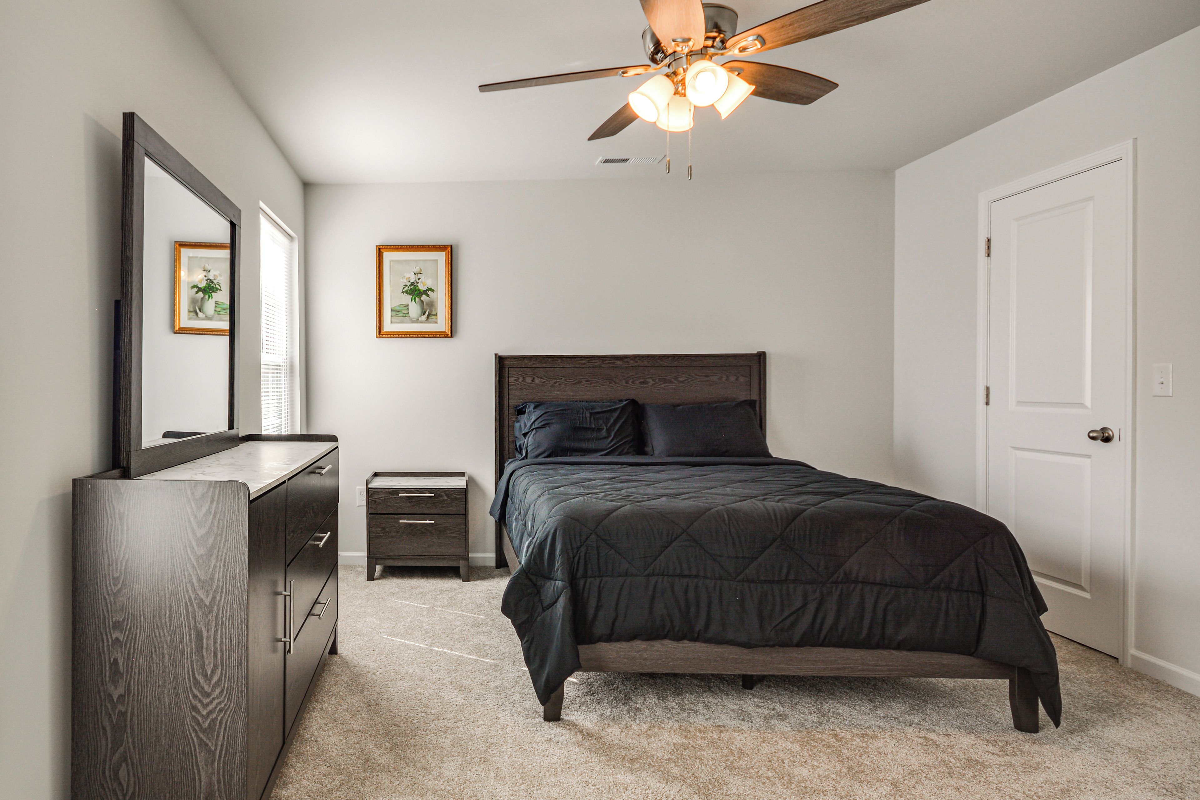 A bedroom with a bed, dresser, nightstand, ceiling fan, and two framed pictures on the wall.