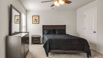 A bedroom with a bed, dresser, nightstand, ceiling fan, and two framed pictures on the wall.