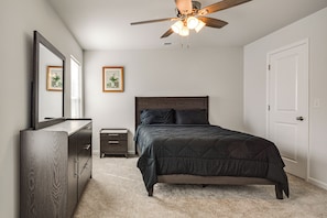 A bedroom with a bed, dresser, nightstand, ceiling fan, and two framed pictures on the wall.