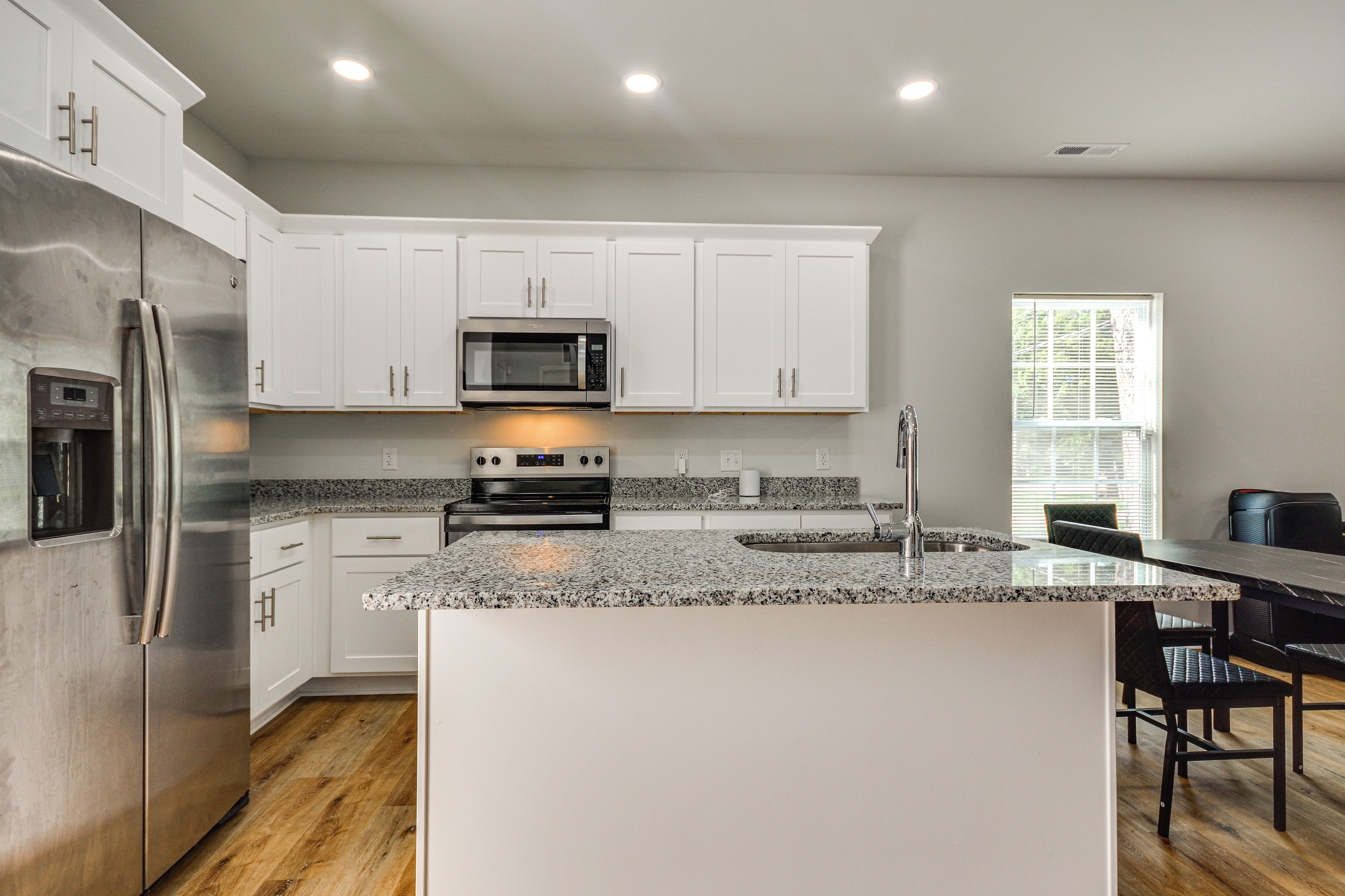 Una cocina moderna con armarios blancos, electrodomésticos de acero inoxidable, encimera de granito y una isla integrada con taburetes de bar.