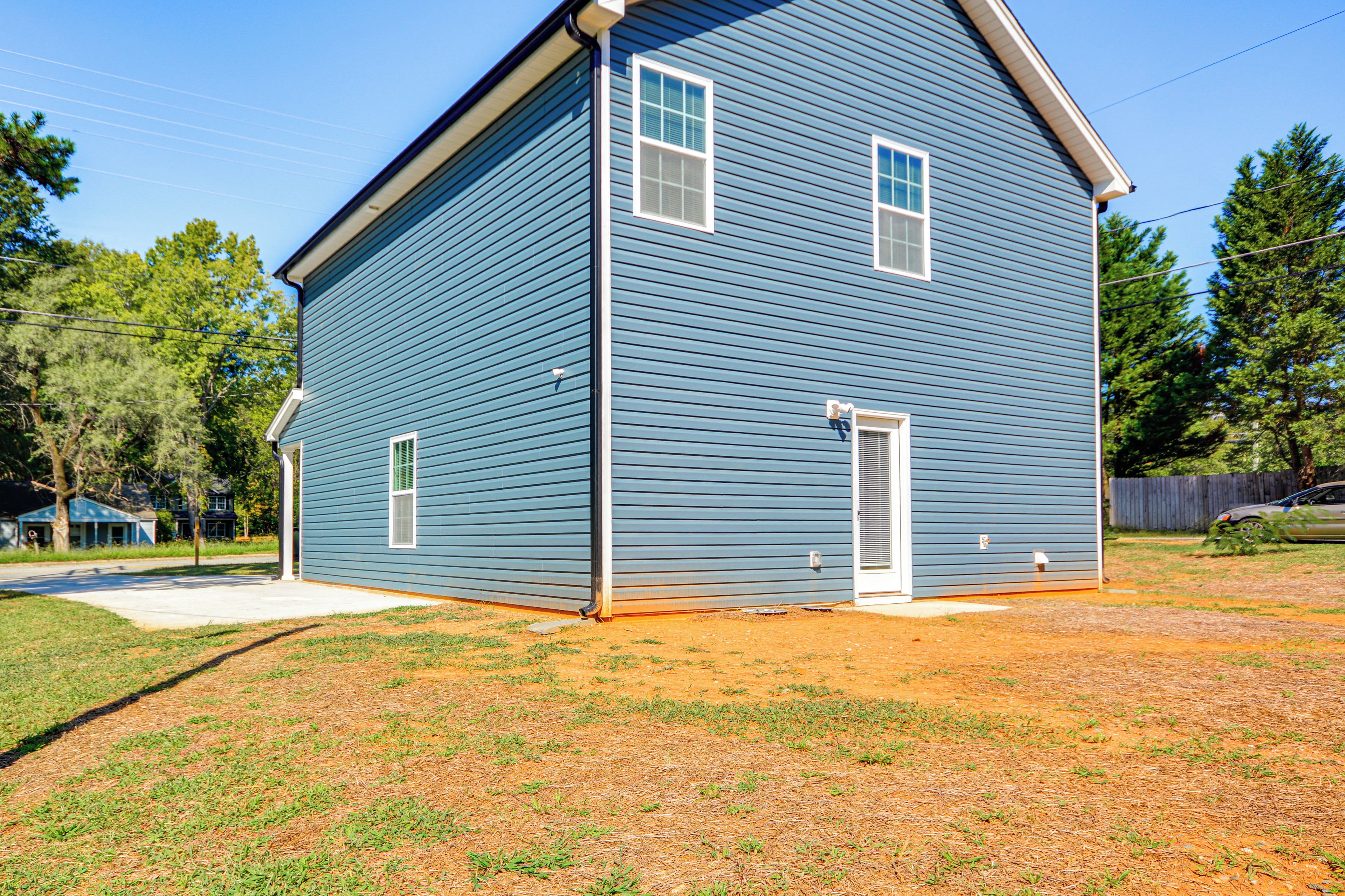A two-story residential building with a gabled roof, a front porch, and a small front yard with grass and a dirt patch.