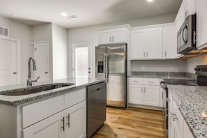 A modern kitchen with white cabinets, a stainless steel refrigerator, and granite countertops.