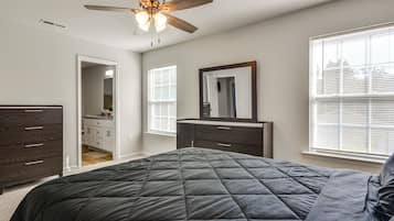 Een slaapkamer met een bed, een dressoir, een spiegel, een plafondventilator en een raam met jaloezieën.