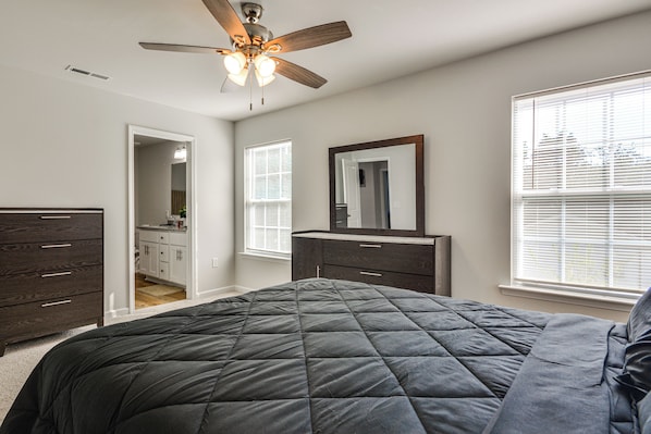 A bedroom with a bed, a dresser, a mirror, a ceiling fan, and a window with blinds.