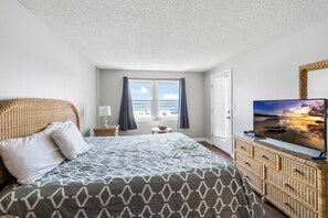 Ett hotellrum med en säng, en tv, en byrå av rotting och ett fönster med utsikt över stranden.