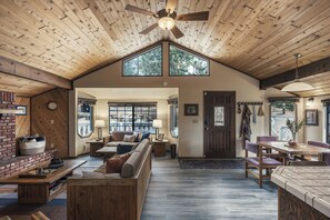 A spacious living area with a high ceiling, a fireplace, a seating area with a sofa and a coffee table, and a dining area with a table and chairs. - Big Bear Cabin w/ EV Charging, Fireplace & Deck! (Sugarloaf)
