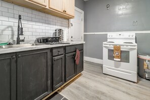A kitchen with a white stove, a sink, and dark cabinets. - Quaint Apt 6 Mi to Stadiums & Dtwn Detroit! (Detroit)