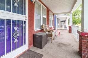 A covered porch with outdoor seating, a brick wall, and a security camera. - Quaint Apt 6 Mi to Stadiums & Dtwn Detroit! (Detroit)