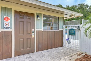 A building with a brown door, a window with a metal grill, and a white fence with a sign.