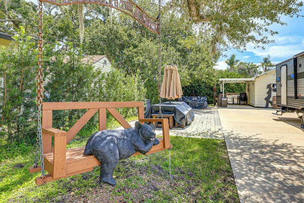 A backyard with a swing set, outdoor furniture, and a grill area.
