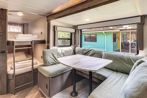 Interior compacto de una caravana con kitchenette, comedor y una litera.