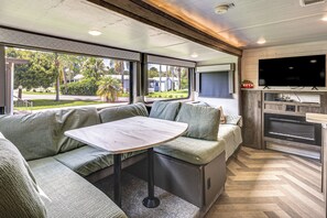 Un interior de autocaravana moderno con comedor, asientos, televisión y zona de cocina.
