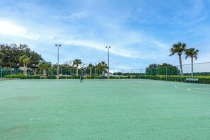 An outdoor tennis court with a green surface, surrounded by a fence, palm trees, and street lamps. - River Ranch RV Retreat w/ Pool & Hot Tub Access (River Ranch)