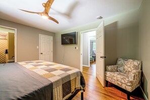 Ein Schlafzimmer mit einem Bett, einem Sessel, einem Deckenventilator, einem Fernseher und einer Tür zu einem anderen Raum.