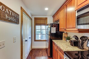 A kitchen with wooden cabinets, a black refrigerator, a microwave, and a window with blinds.