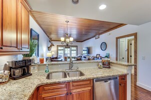 Una cocina con encimeras de granito, armarios de madera, lavavajillas de acero inoxidable y techo con vigas de madera.