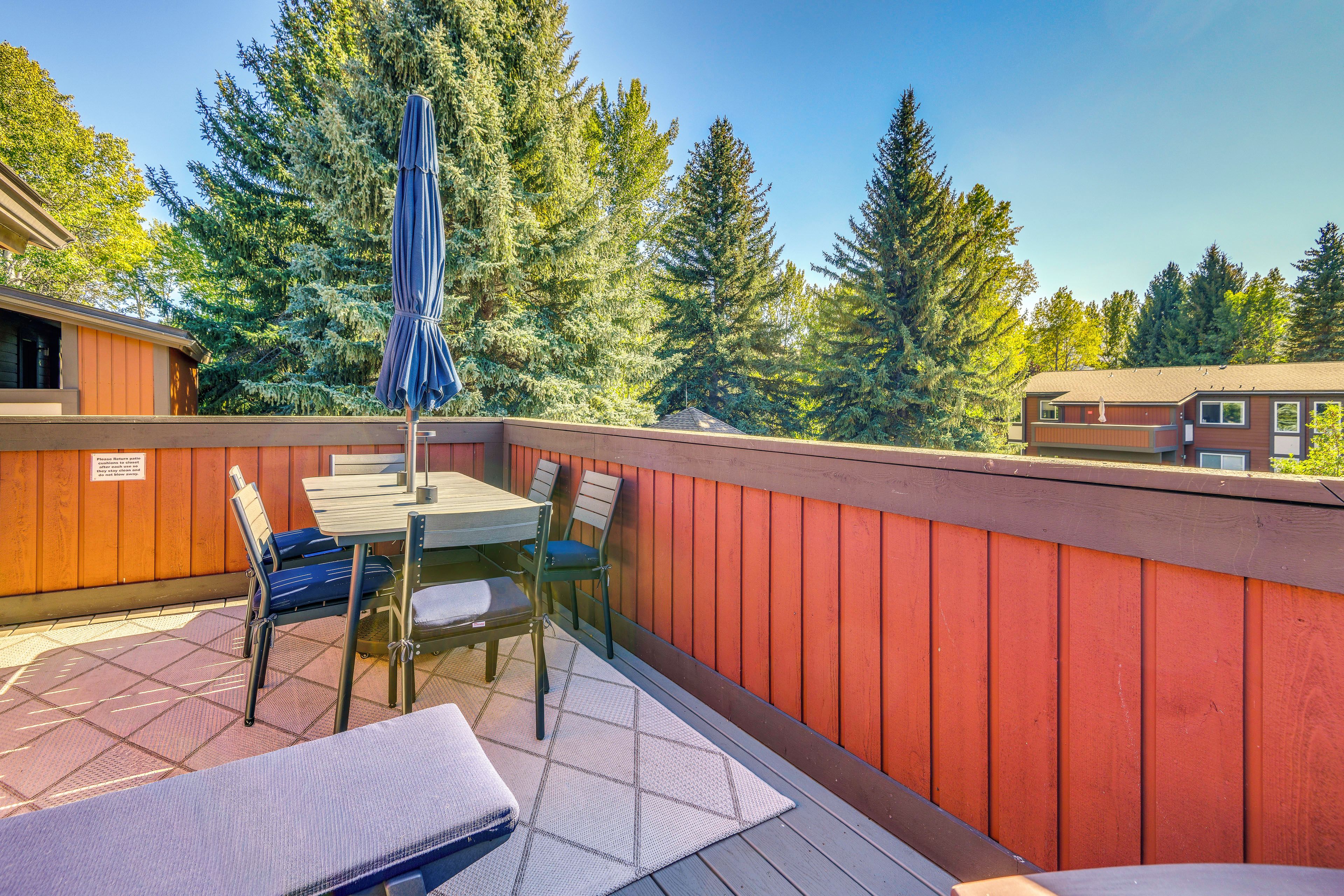 A patio area with a table and chairs, a covered umbrella, and a view of surrounding trees.