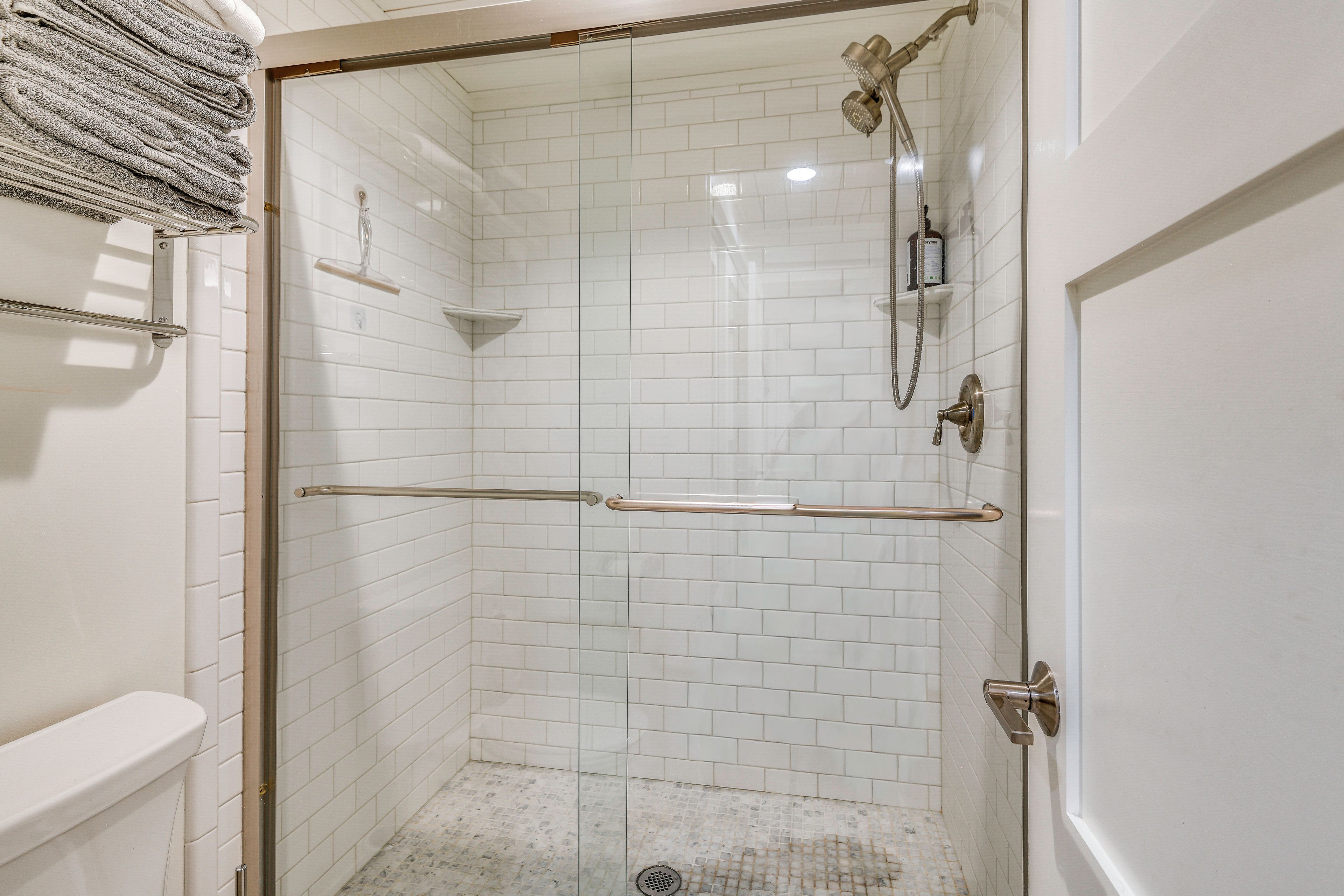 A walk-in shower with white tiled walls, a glass door, and a metal showerhead.