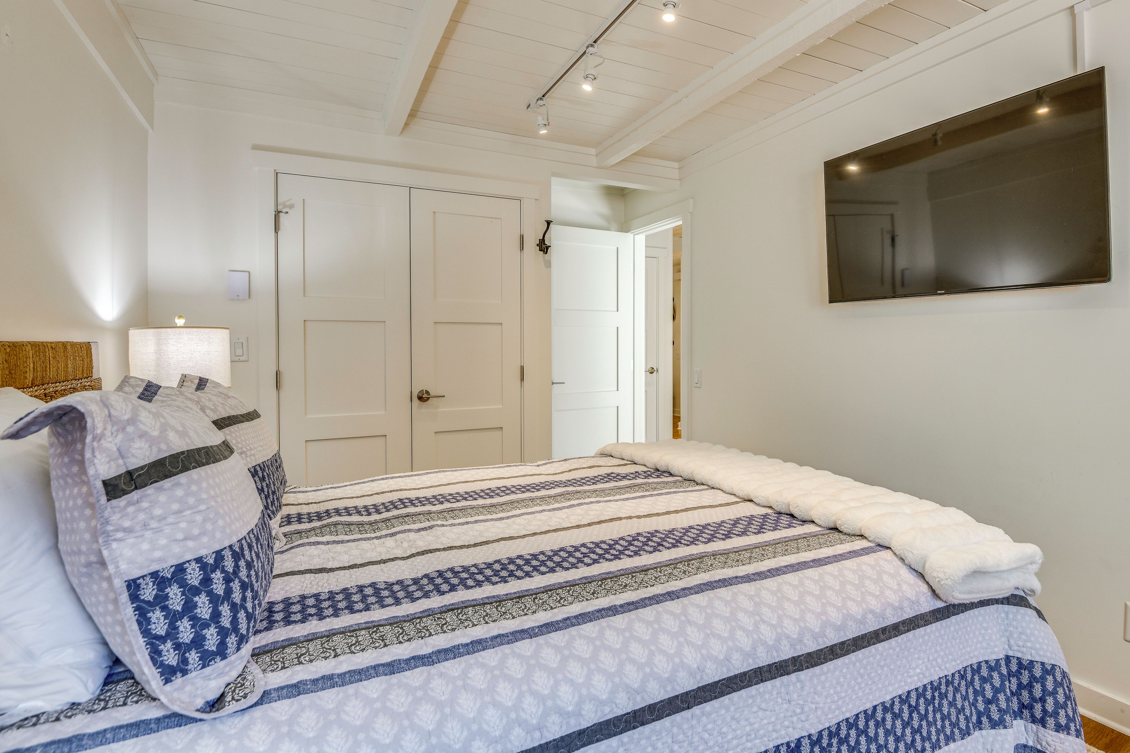 A bedroom with a bed, a TV mounted on the wall, and a door leading to another room.