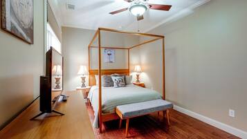 A four-poster bed with a wooden frame, two bedside tables with lamps, a ceiling fan, and hardwood flooring.