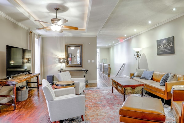 A spacious living room with a ceiling fan, a flat-screen TV, a coffee table, a sofa, and a patterned rug.