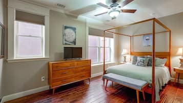 A bedroom with a four-poster bed, a dresser, a television, and a ceiling fan.
