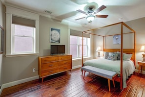 A bedroom with a four-poster bed, a dresser, a television, and a ceiling fan.