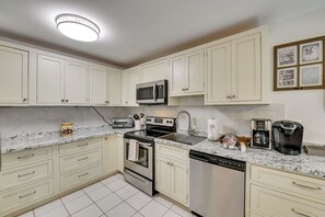 Una cocina con gabinetes blancos, microondas, tostadora, cafetera y lavavajillas.