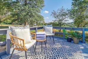 An outdoor deck with wicker chairs and a table, surrounded by a railing and a patterned floor. - Fire Pit & Fenced Yard! Peaceful Glen Carbon Home (Glen Carbon)