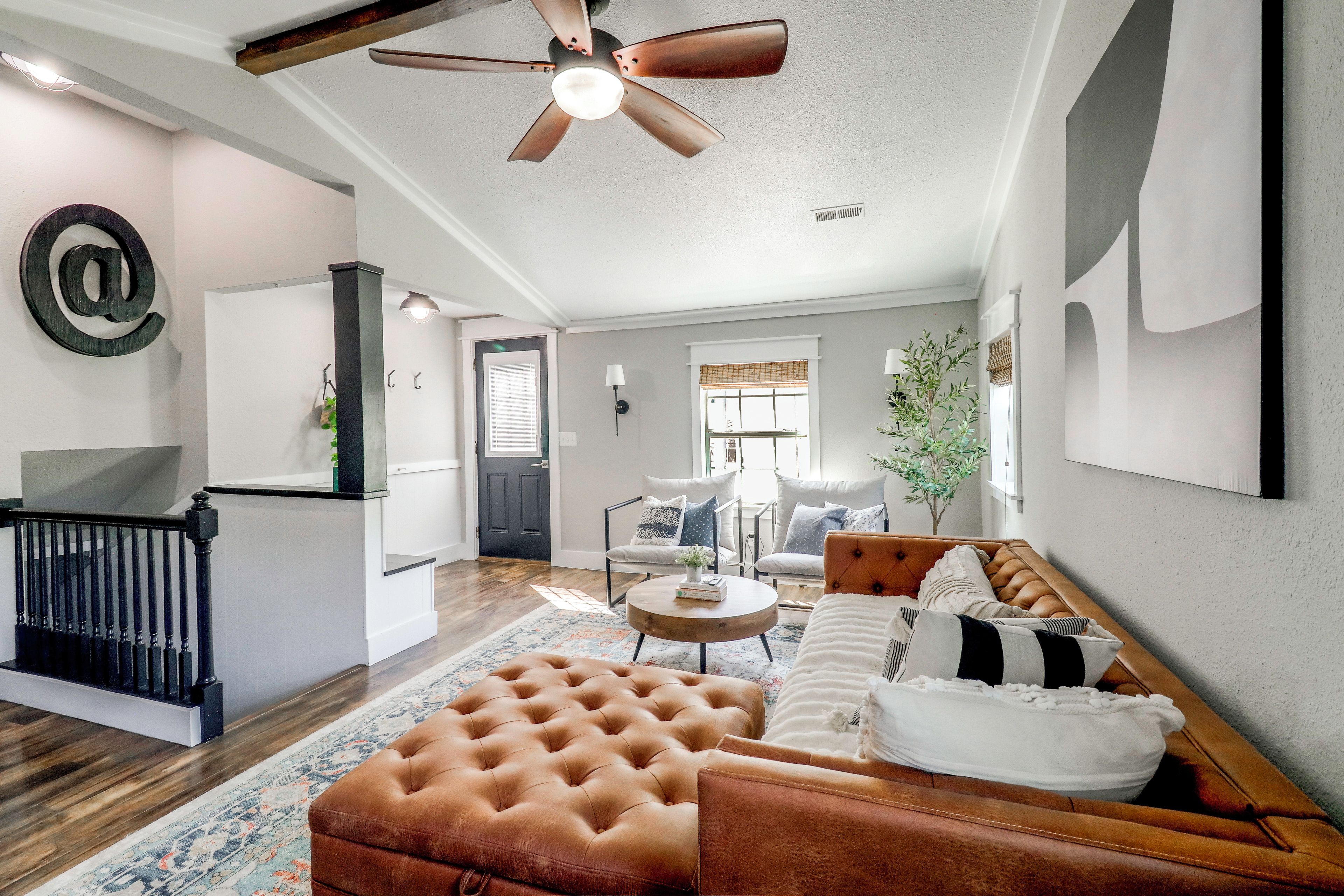 A spacious living room with a brown leather sofa, a round coffee table, and a ceiling fan.