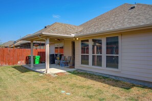 A residential house with a covered patio, a fenced yard, and a visible trash bin.