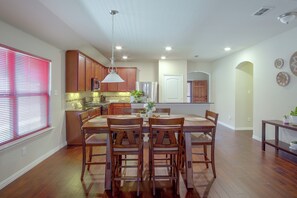 A spacious kitchen with wooden cabinets, a dining area with a wooden table and chairs, and a hallway leading to a door.