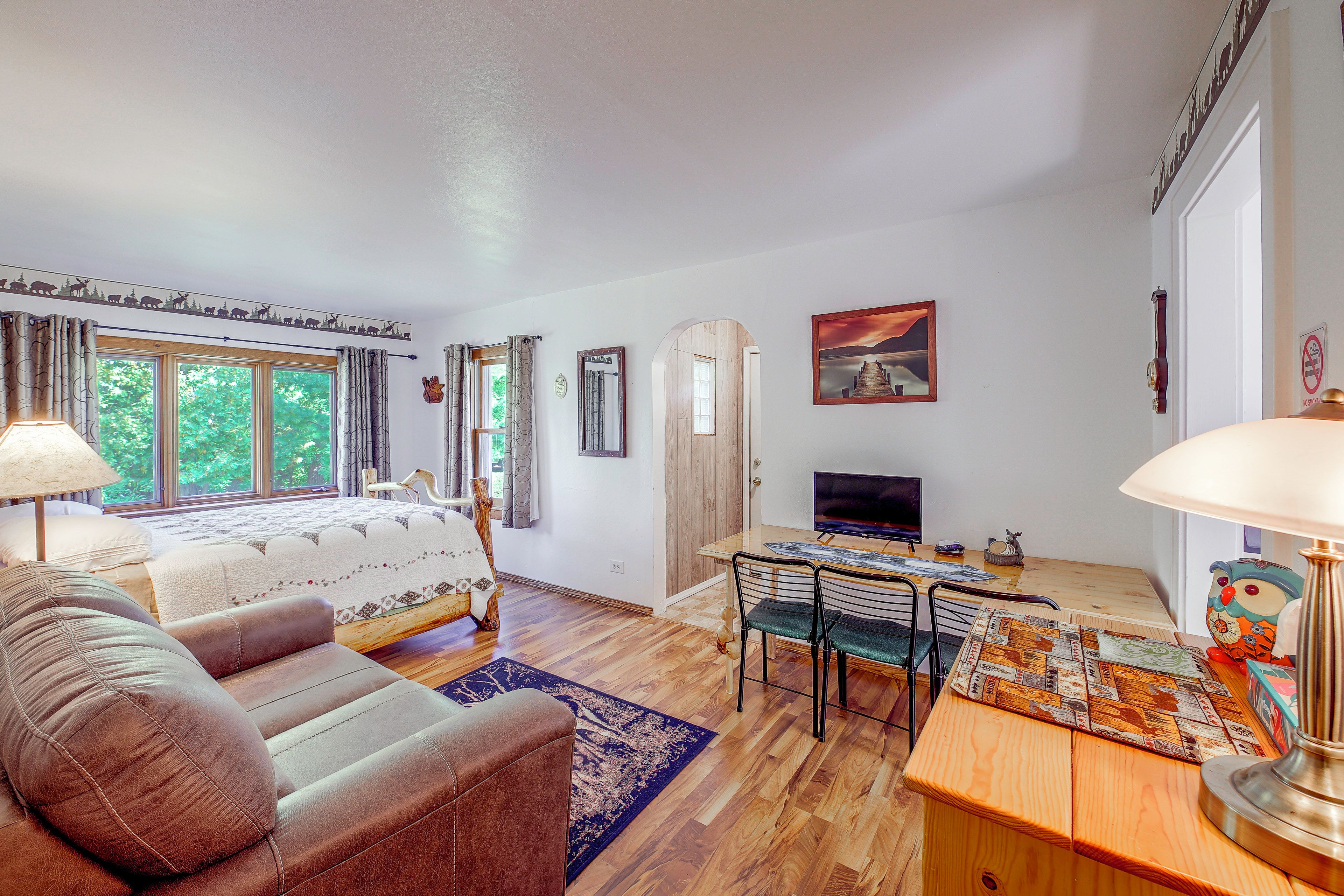 A bedroom with a bed, a desk, a chair, a TV, and a window.