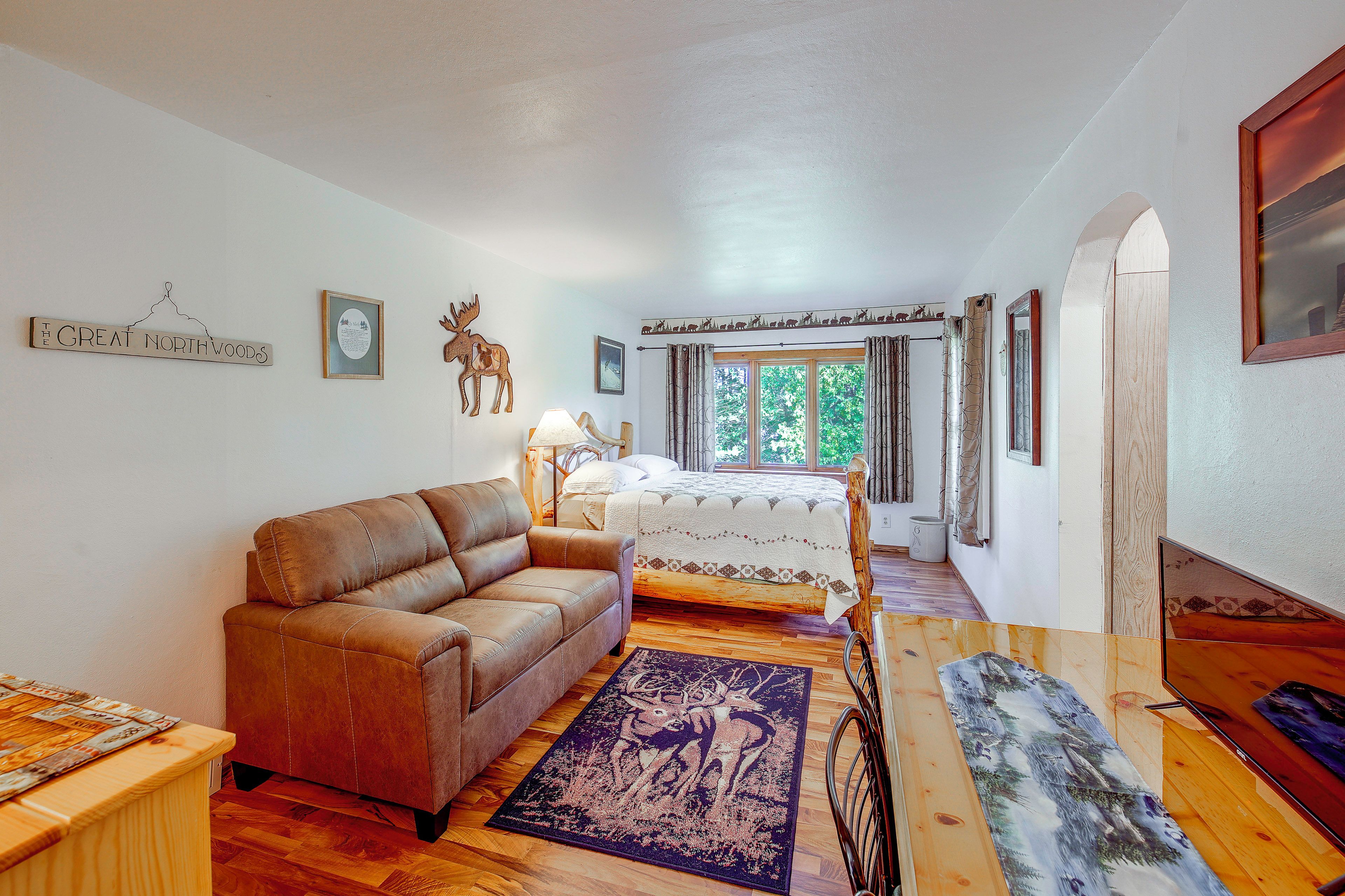 Una habitación con sofá de cuero marrón, cama con cabecera de madera, ventana con cortinas y una pared con un cuadro y un letrero.