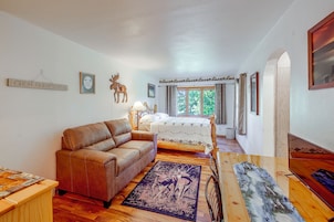 A room with a brown leather sofa, a bed with a wooden headboard, a window with curtains, and a wall with a mounted picture frame and a sign.