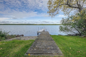 A wooden dock leading to a small pier extending into a calm lake, surrounded by grassy banks and trees. - Paddle, Fish & Unwind: Shagawa Lake Home (Ely)