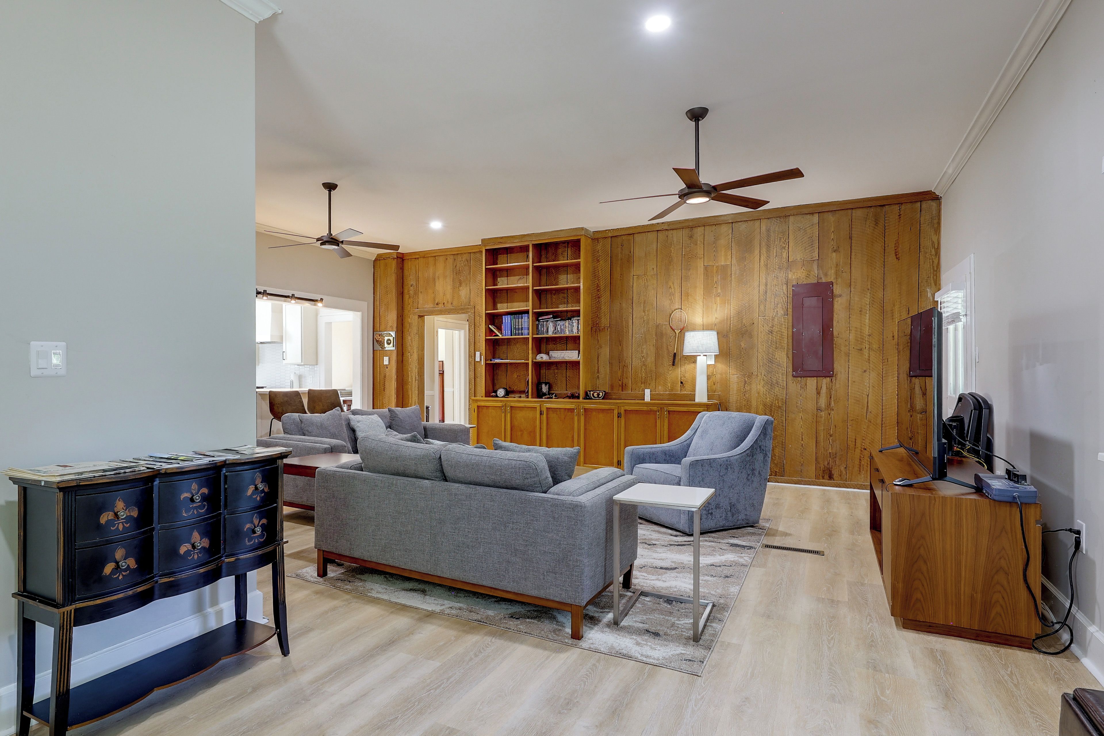 A spacious living room with a sofa set, a wooden bookshelf, and a ceiling fan.