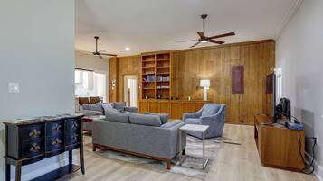 A spacious living room with a sofa set, a wooden bookshelf, and a ceiling fan.