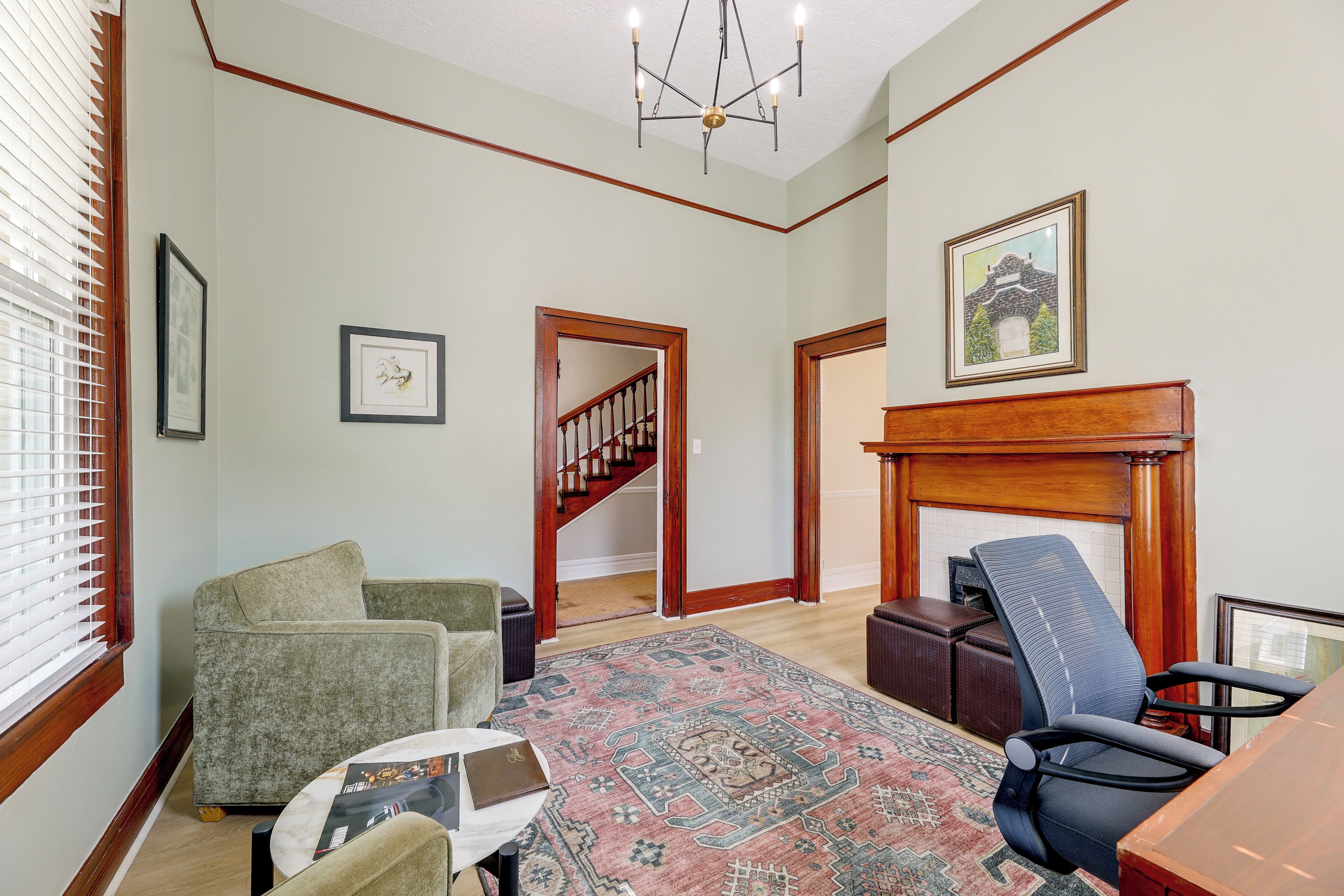 A spacious living room with a fireplace, a staircase, and a large window with blinds.