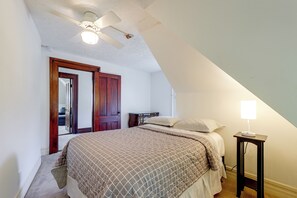 A bedroom with a bed, a nightstand, a lamp, a ceiling fan, and a door leading to another room. - Tuskegee 5BR Home in Historic District (Tuskegee)