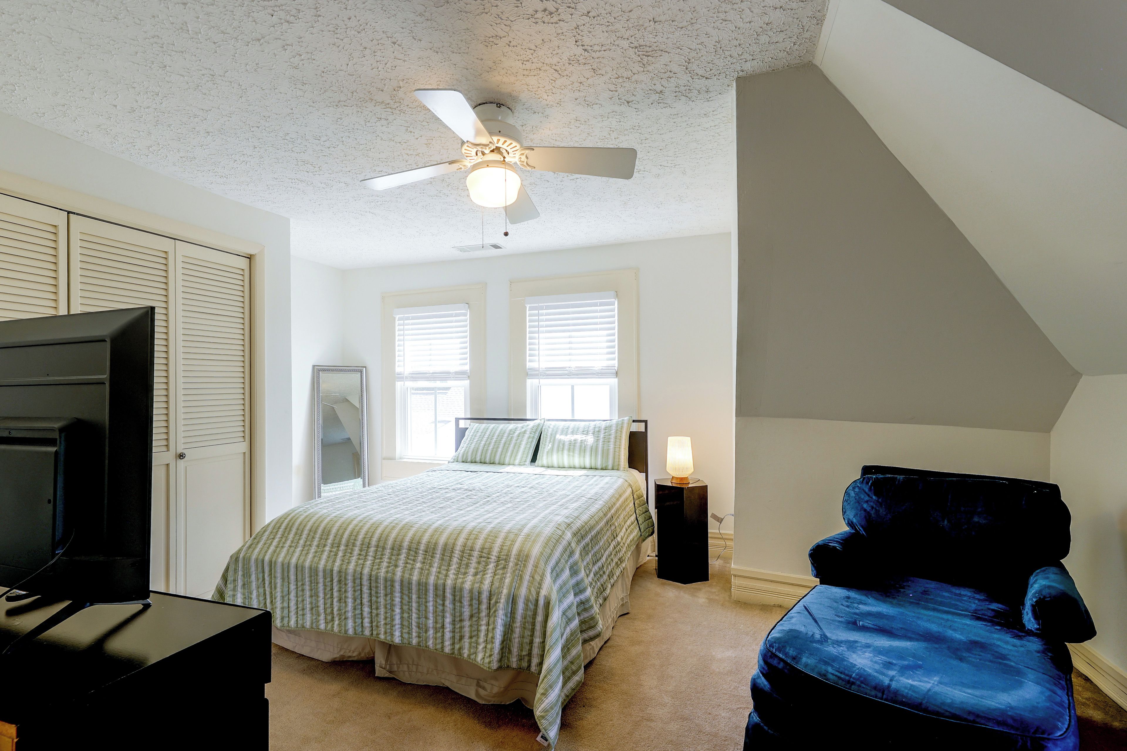 Ein Schlafzimmer mit Bett, Fernseher, Deckenventilator und Fenster.